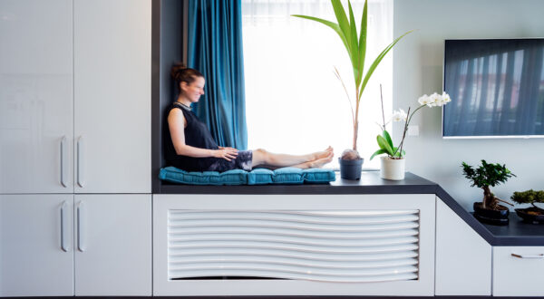 Žena sedi u prozorskoj niši savremenog enterijera.