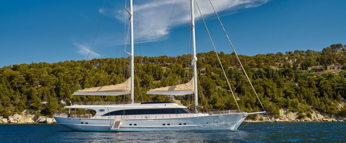 Two-masted luxury sailing yacht near a forested coastline