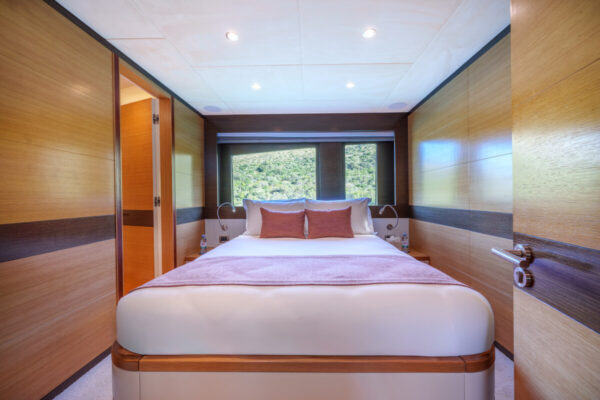 Double cabin of the Silent World yacht with a large bed and wooden paneling in two shades